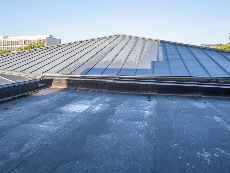 Single-ply membrane flat roof with a metal roof behind