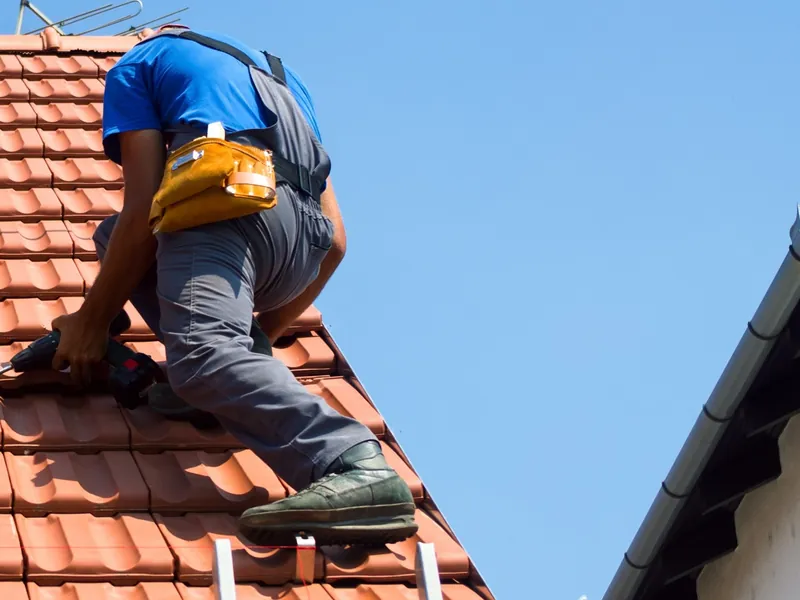 Roofer kneeling on a clay tiled roof carrying out repairs